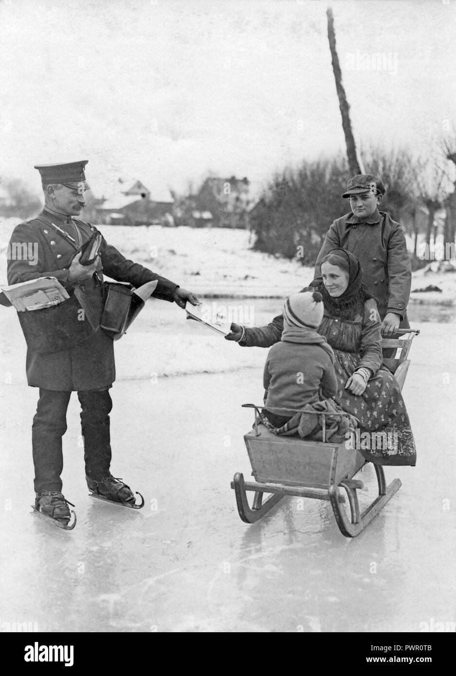 Skating mail man. A properly dressed mailman in uniform is delivering the post when skating on the ice. A woman sitting in a sledge reaches for her post. 1930s. Stock Photo