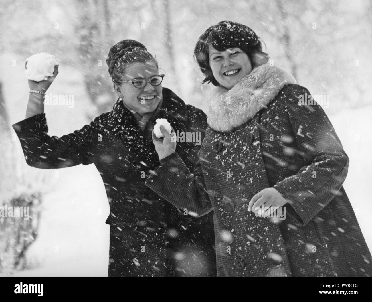 Winter in the 1960s. Two young women is aiming and about to throw snowballs at the photographer. The snow is falling and they are dressed warm with winter coats. Sweden 1964 Stock Photo