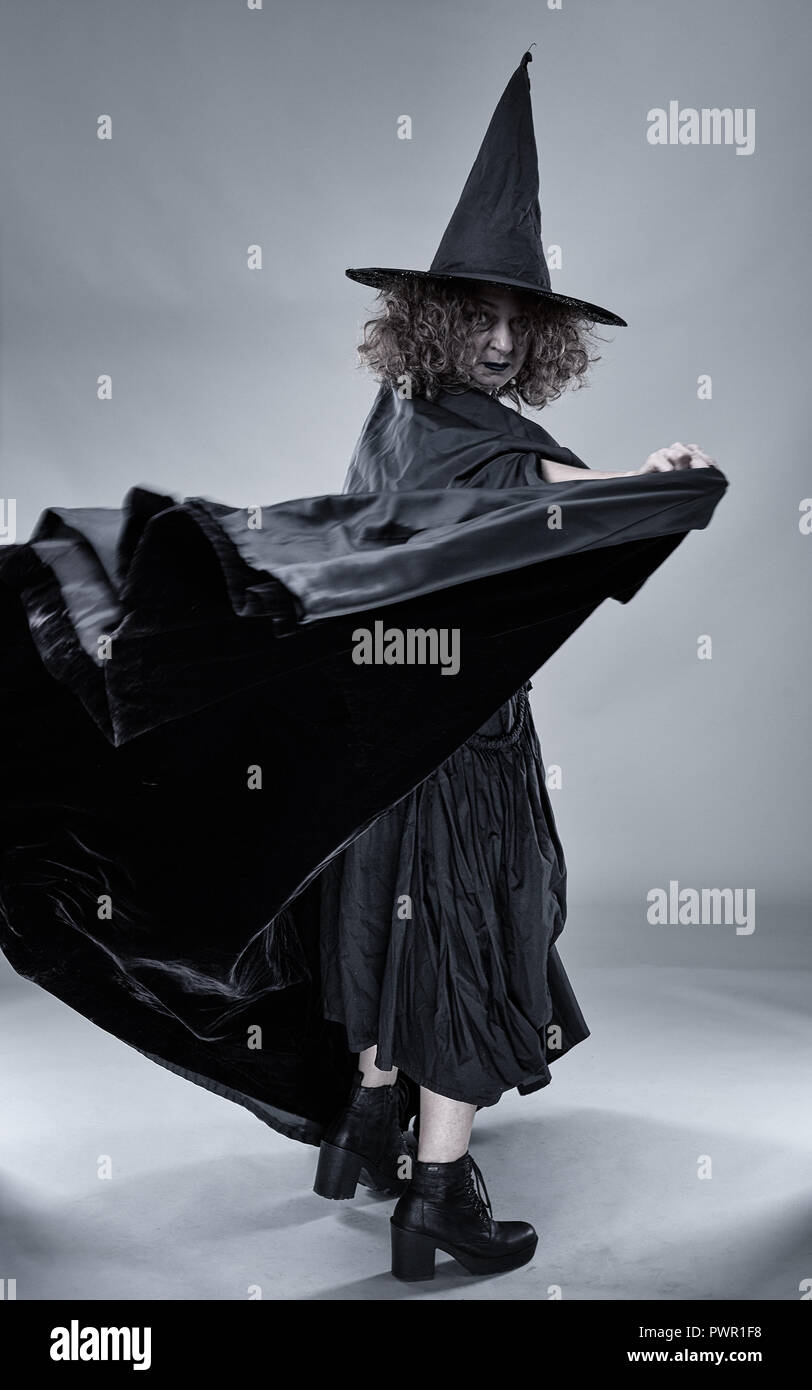 Old witch in black cape and hat against gray background Stock Photo - Alamy