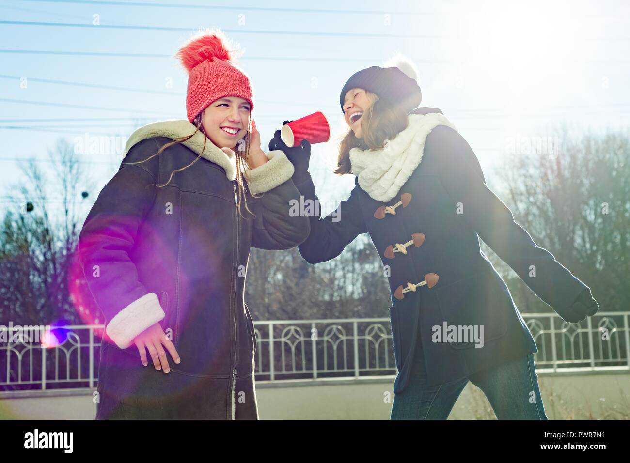 Girls teens shout into a megaphone paper cup, dressed in winter clothes ...