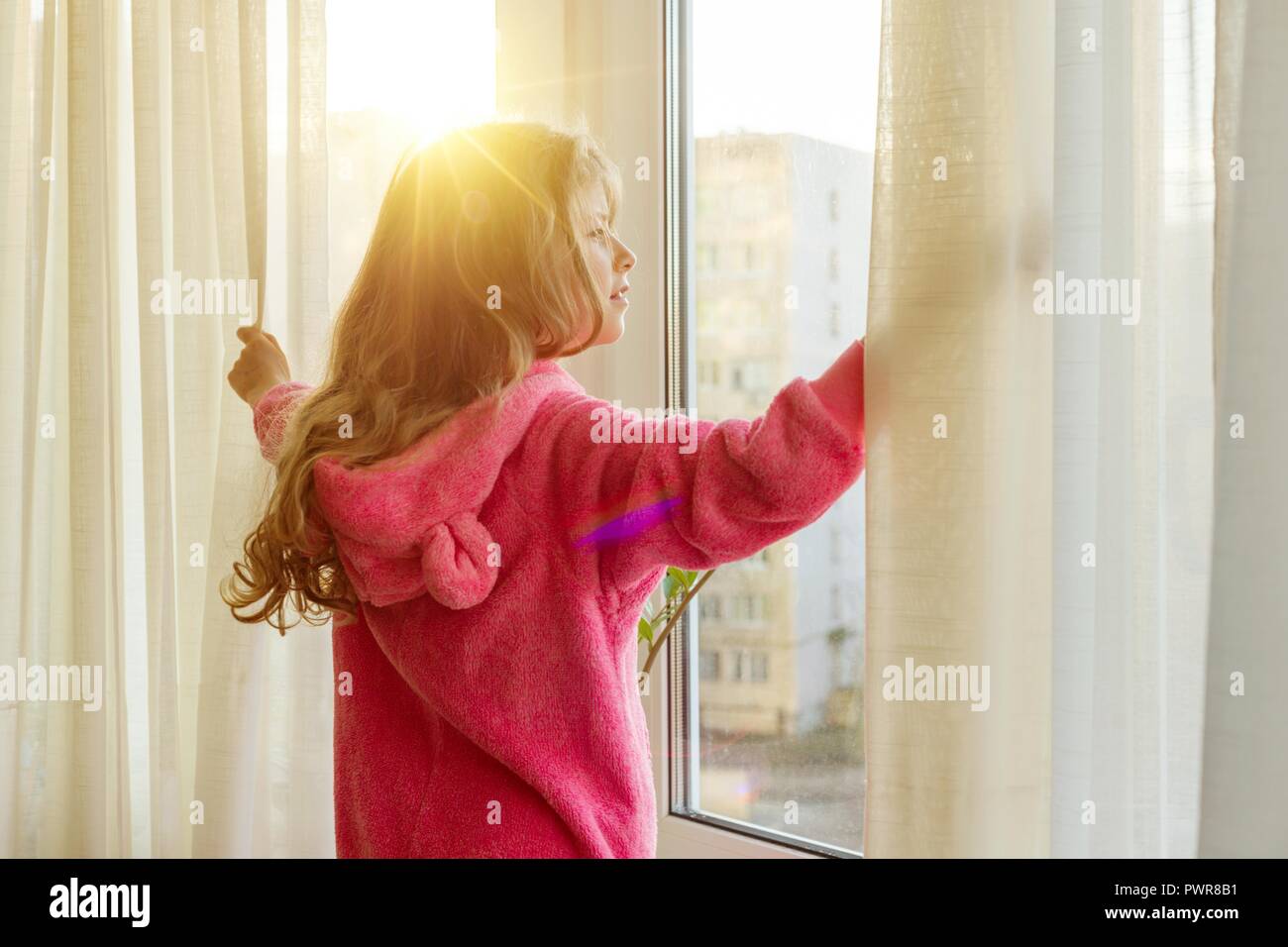 Good Morning Girl Child In Pajamas Opens Curtains And Looks Out