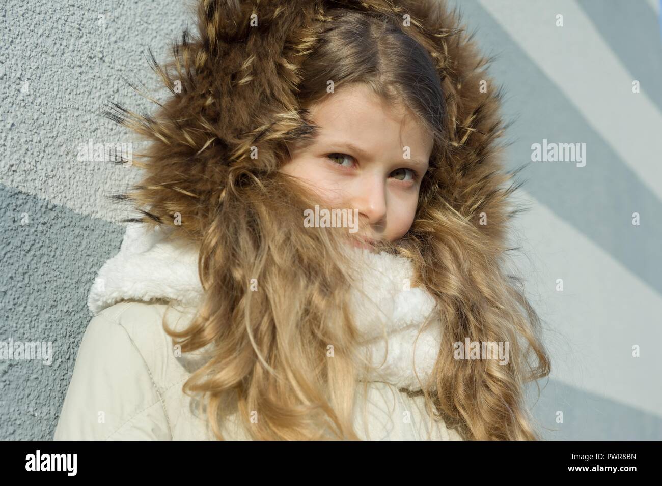 Close-up of an outdoor winter portrait of child, blonde girl with curly hair of 7,8 years in fur hood. Stock Photo
