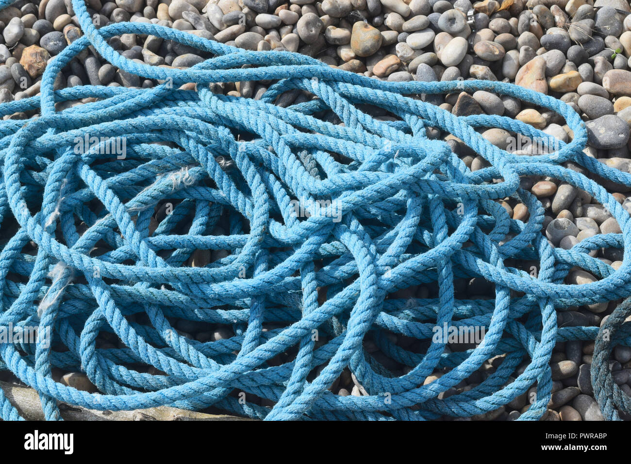 Coiled-up blue rope lying on pebble beach Stock Photo