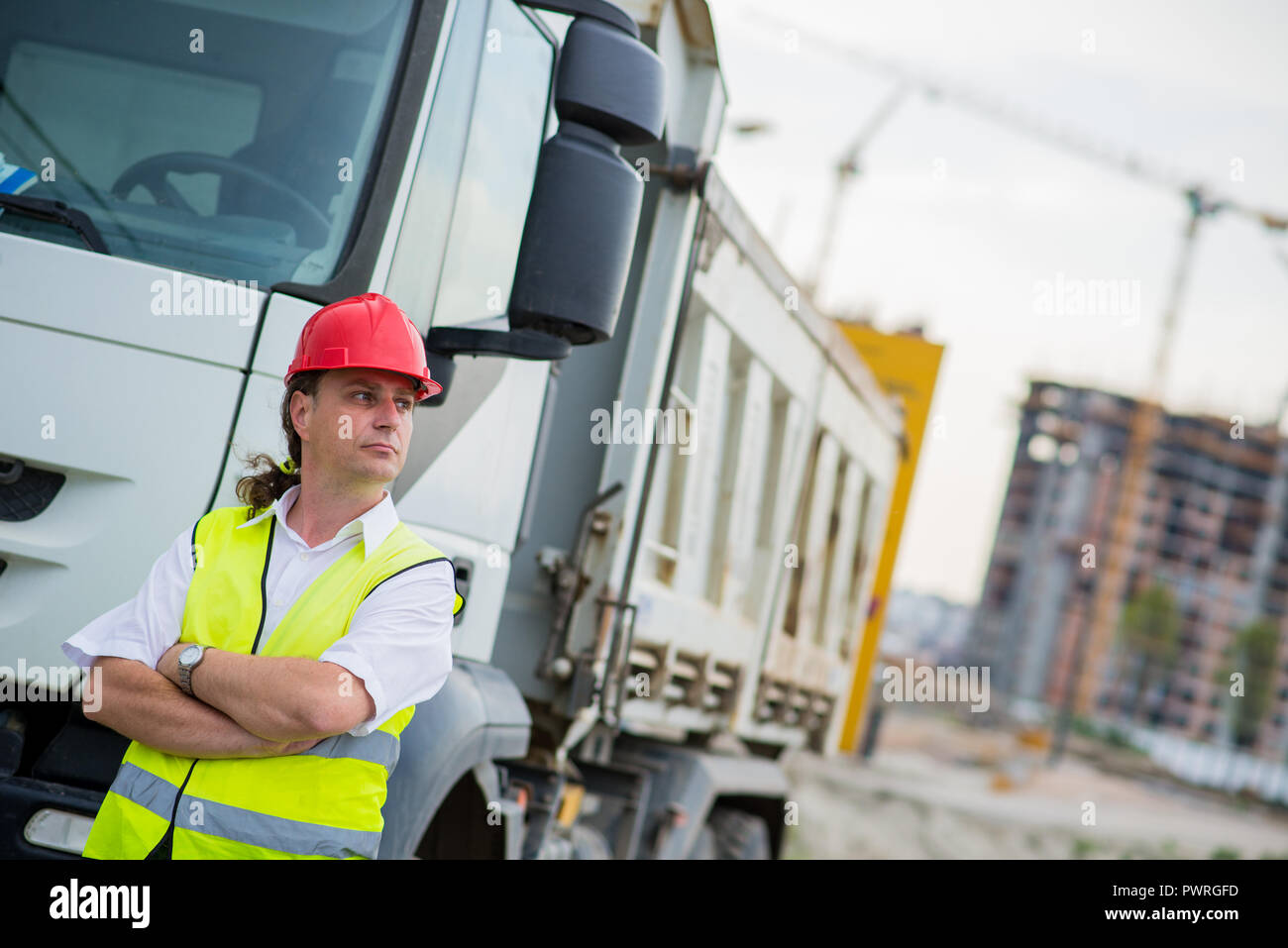 Truck driver in front of a truck on a construction site with his arms