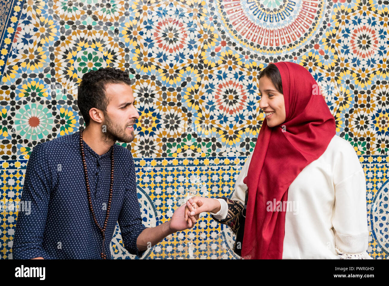 Young Muslim couple in relationship talking and smiling holding hands in front of arabesque oriental decoration Stock Photo