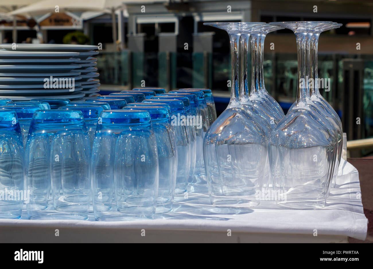 Blue tinted tumblers and wine glasses with plates stacked in a restaurant on the marina in Vilamoura Portugal Stock Photo