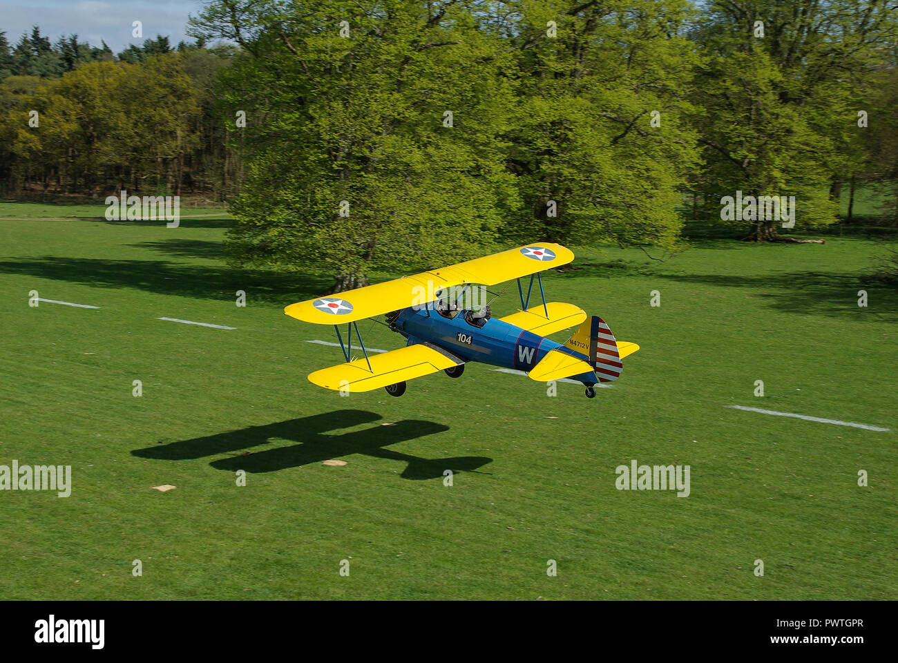 Boeing Kaydet biplane N4712V, trainer plane taking off from Henham Park countryside grass strip. Tree lined Suffolk grass runway on sunny day Stock Photo