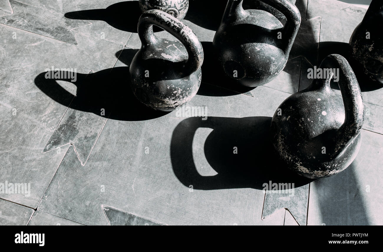 Old scratch dumbbells on a rubber surface in gym in sunlight. Stock Photo