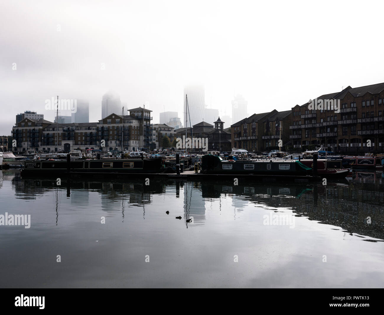 Low cloud hides the top of the tall buildings at Canary Wharf as seen from Limehouse Basin in East London Stock Photo