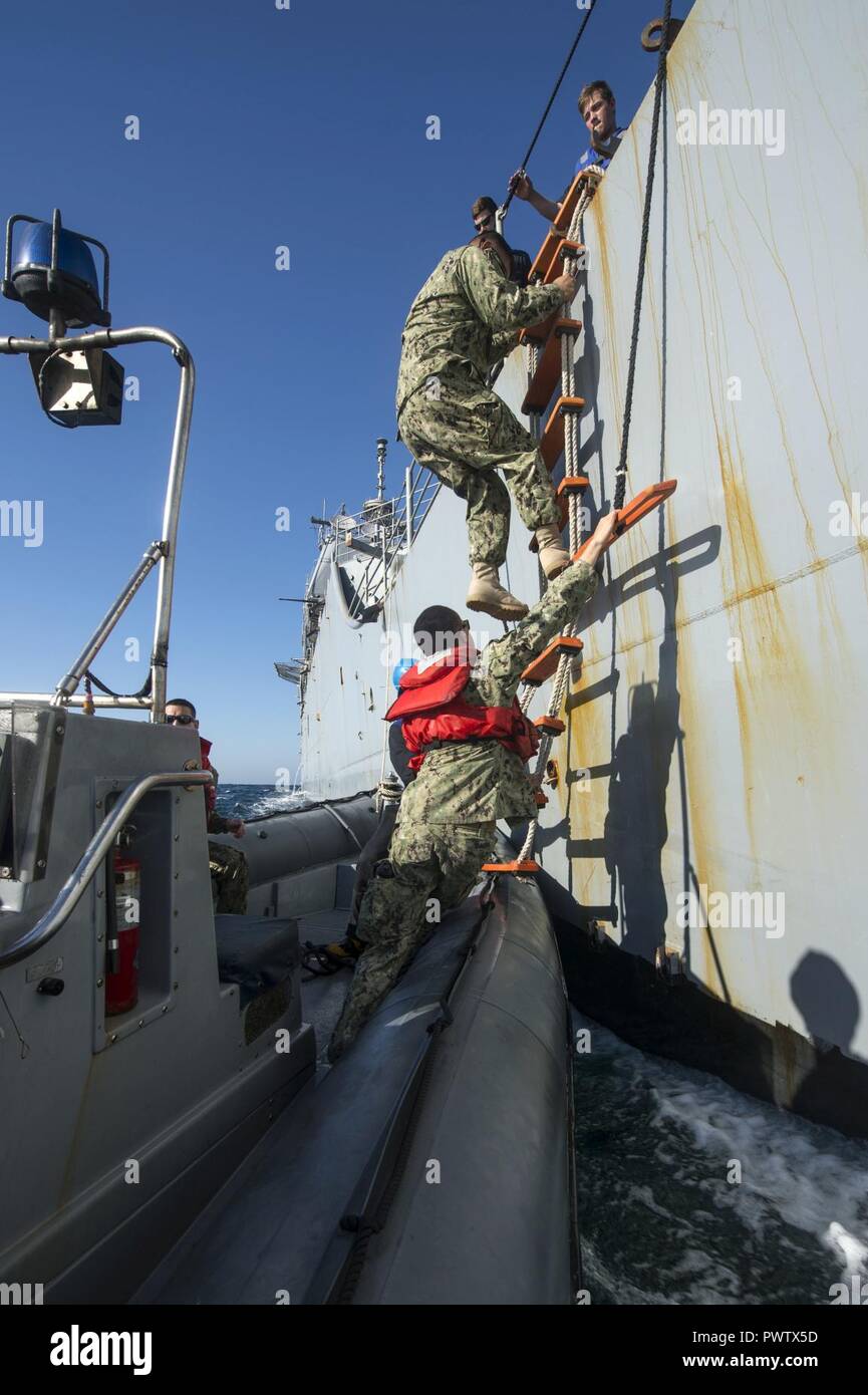 ARABIAN GULF (June 20, 2017) Mass Communication Specialist 2nd Class Austin Simmons, assigned to Expeditionary Combat Camera, stabilizes a pilot’s ladder as Capt. Leo Albea, deputy commodore of Destroyer Squadron (DESRON) 50, disembarks the guided-missile cruiser USS Vella Gulf (CG 72) onto a rigid-hull inflatable boat for transfer to the coastal patrol ship USS Firebolt (PC 10) e Exercise Spartan Kopis 17.  Exercise Spartan Kopis is a Task Force (TF) 55-led exercise between the U.S. Navy and U.S. Coast Guard in order to increase tactical proficiency, broaden levels of cooperation, enhance mut Stock Photo