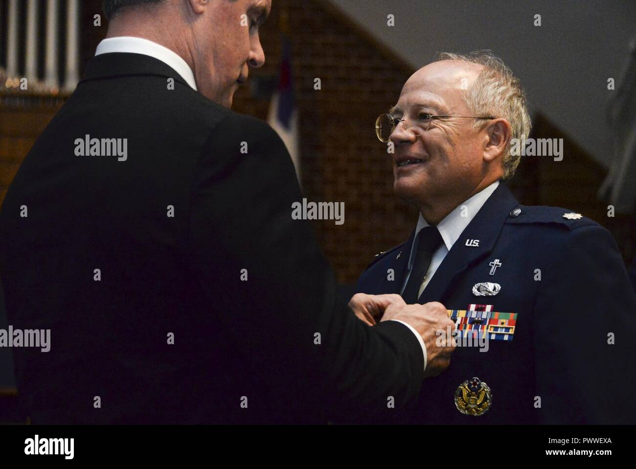 John A. Weida, Director of Policy, Programs & Strategy, International Affairs, Office of the Under Secretary of the Air Force (International Affairs), places a Meritorious Service medal onto Lt. Colonel James M. Glass, 70th Intelligence, Surveillance, and Reconnaissance Wing, senior Air Force chaplain, during Glass’ retirement ceremony July 5, 2017 Bowie, Md. Glass received his commission from the US Air Force Academy in 1977. He served as a Communications Maintenance Officer until he separated from the Air Force in May 1982. Glass then re-entered the Air Force as a chaplain in March 1998. Stock Photo