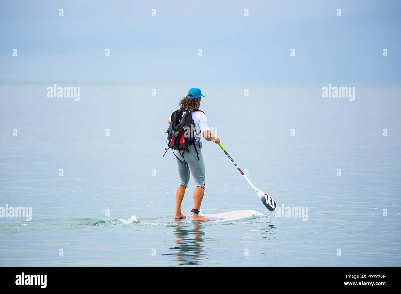 Caucasian male, rear view, isolated in sea, enjoying popular outdoor activity, stand up paddle boarding (SUP surfing) on summer holiday, Wales UK. Stock Photo