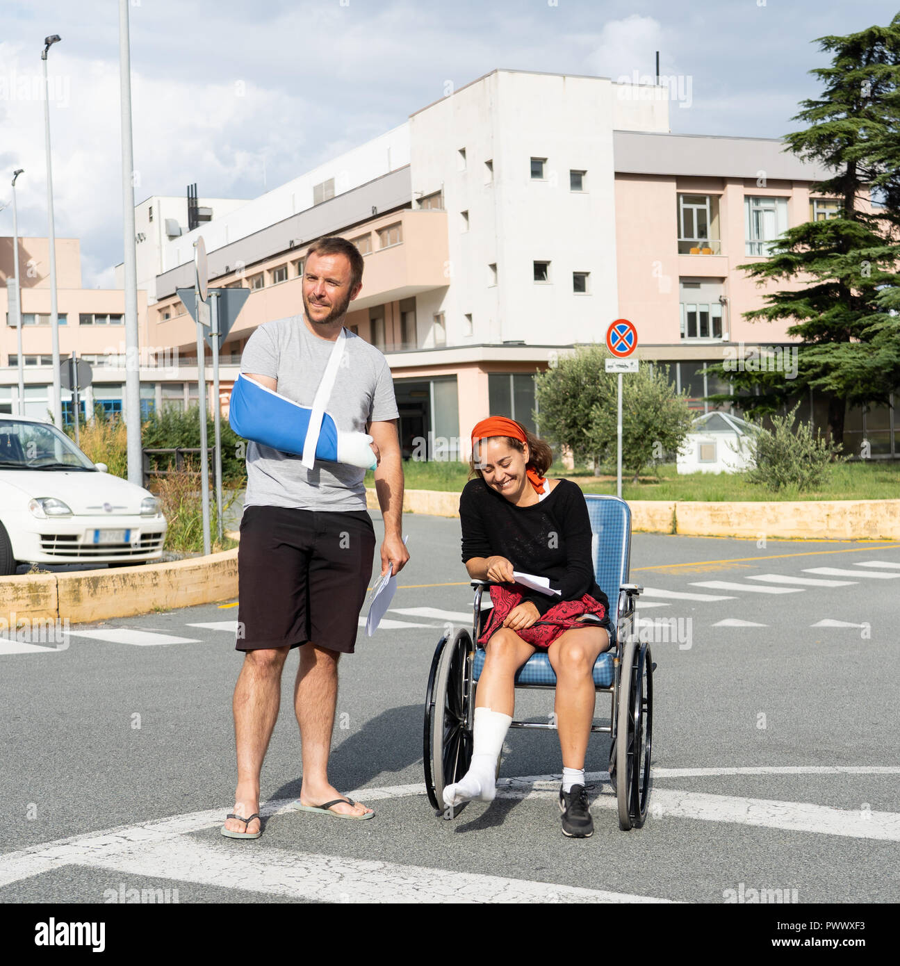 Young injured couple with broken foot and arm coming out of the hospital happy that their insurance paid the medical bills in travel health insurance  Stock Photo