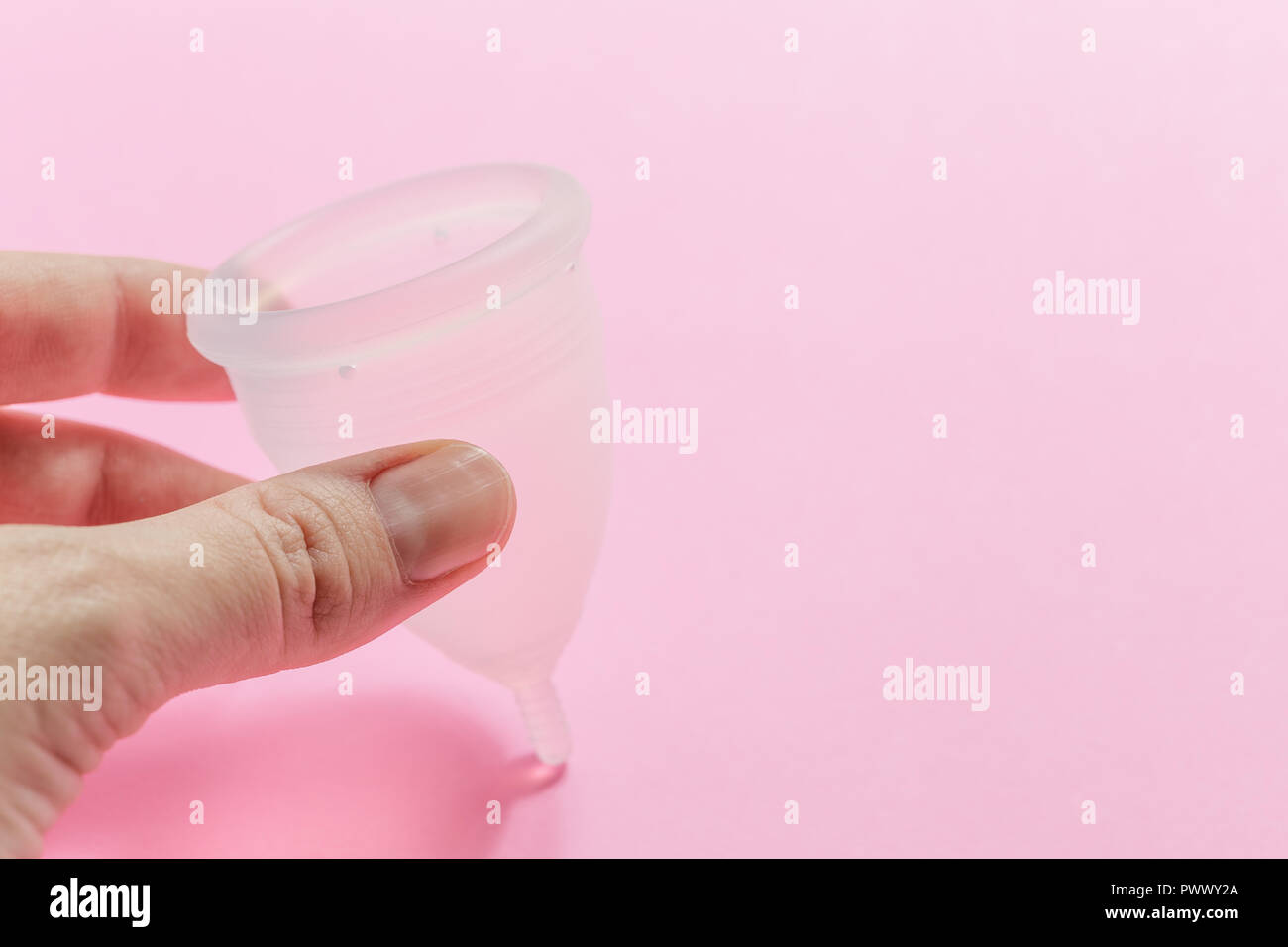 Close up of woman hand holding menstrual cup over pink background. Women health concept, zero waste alternatives Stock Photo