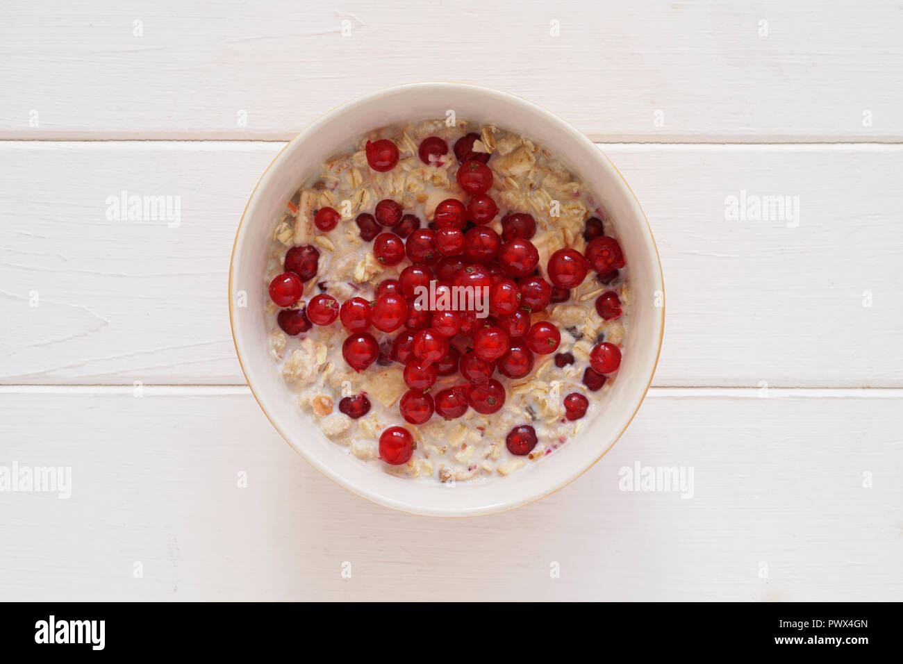 overhead view of breakfast bowl muesli with fresh redcurrant berries on white wooden table Stock Photo