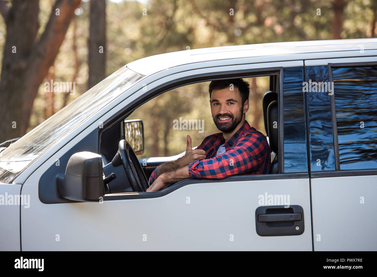 bearded driver showing thumb up while sitting in pickup truck in forest Stock Photo