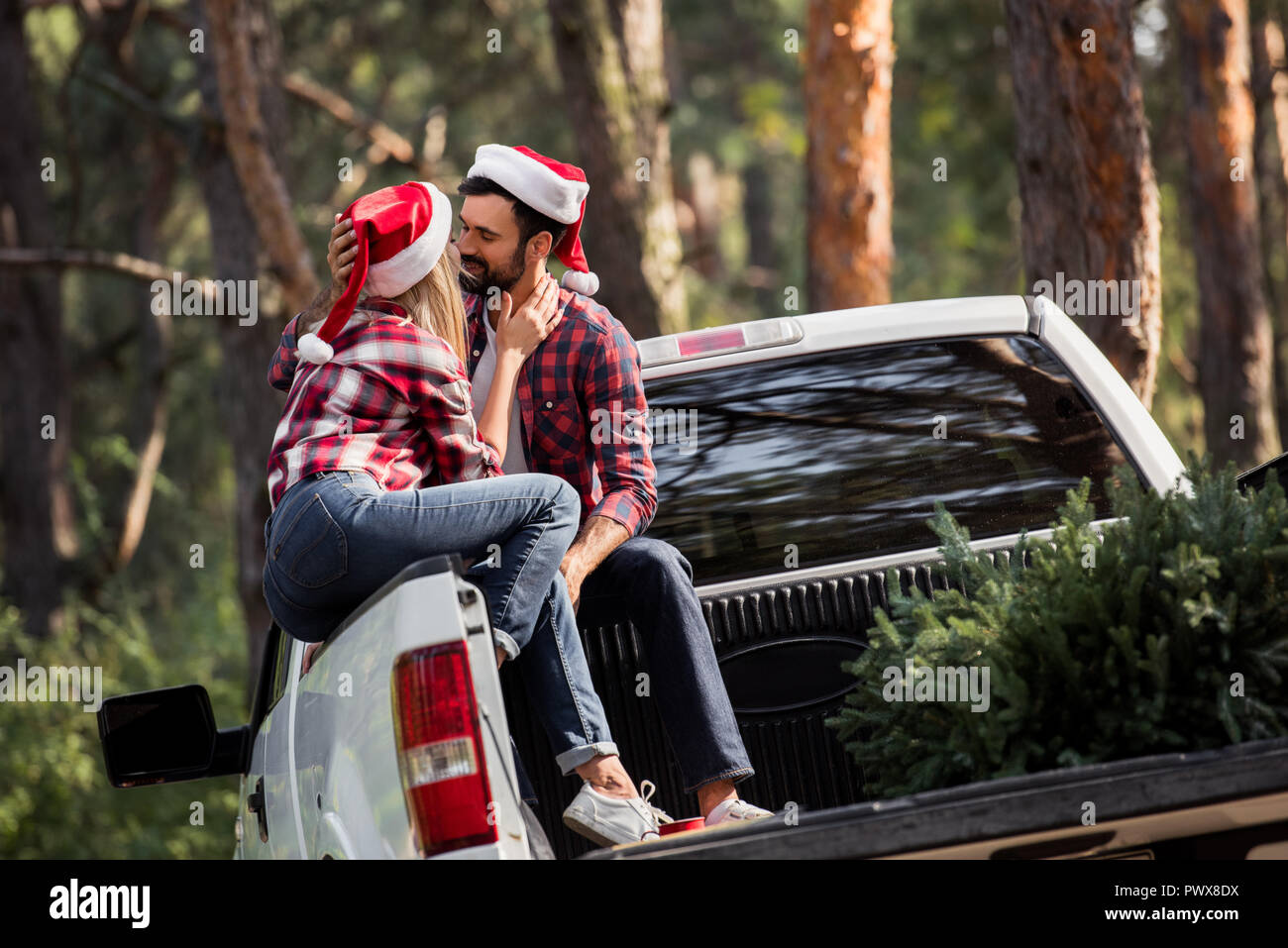 couple in santa hats going to kiss while sitting on pickup truck with