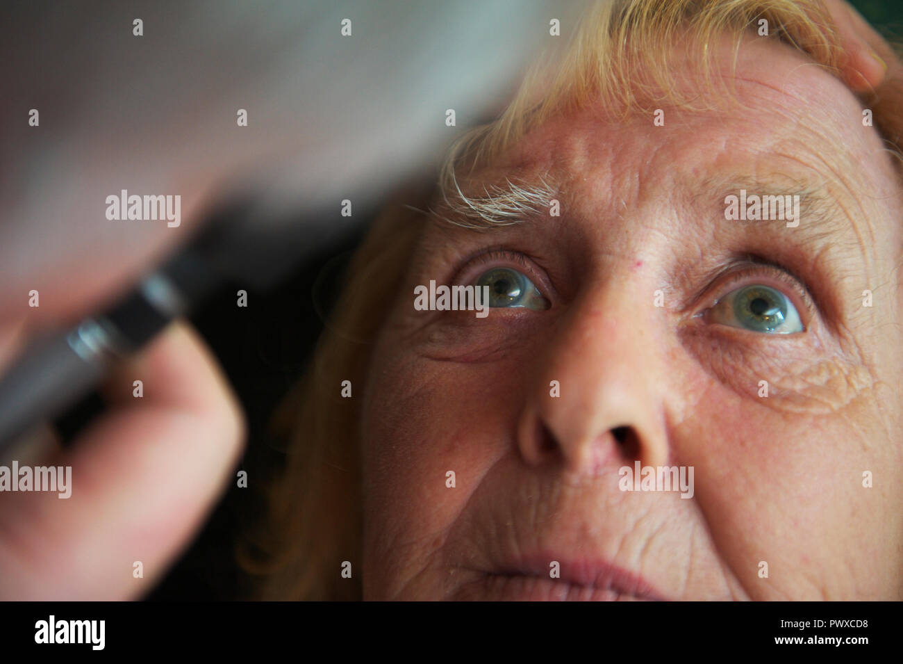 elderly female patient stares at doctors or GP eye examination light during appointment at GP surgery or community visit Stock Photo