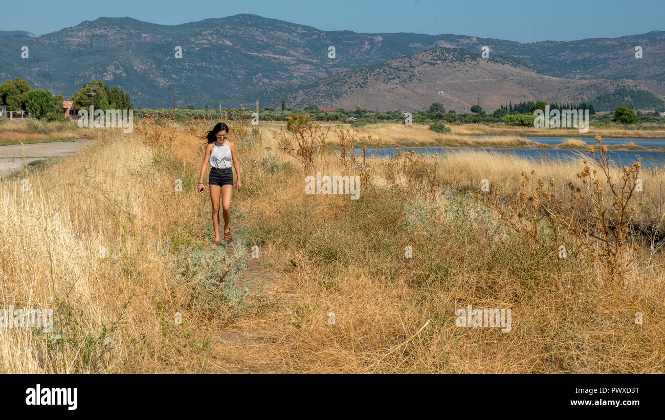Teen walking through the dried grass next to lake with mountains in the background Stock Photo