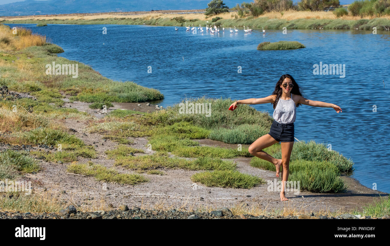 Young girl standing on one leg in front of flamingos Stock Photo