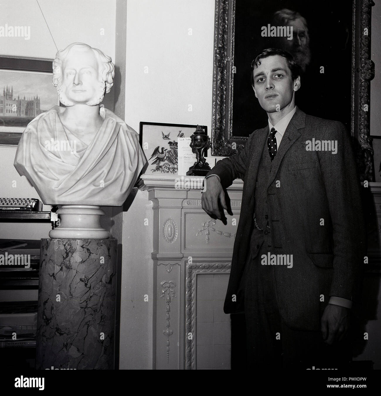 1960s, the 7th Baron Sudeley, Merlin Hanbury-Tracy standing by a bust of one of his forefather's, the likeness of which is apparent. An hereditary peer, Hanbury-Tracy went to Eton and Worcester College, Oxford and was an active member of the House of Lords until the act of 1999 which dramaticaly reduced there the number of hereditary peers. His home, Toddington Manor, a gothic manor house was architecturally the forerunner for the Houses of Parliament. Stock Photo