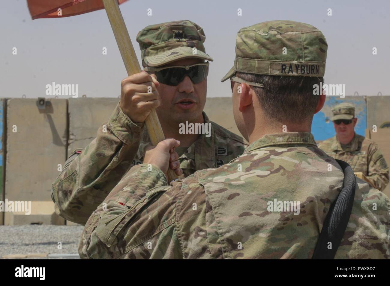 U.S. Army Lt. Col. Sebastian Pastor, commander of 37th Engineer Battalion, 82nd Airborne Division, passes the Alpha Company guidon to U.S. Army Capt. Scott Rayburn, the incoming commander, during a change of command ceremony at Qayyarah West Airfield, Iraq, July 1, 2017. Rayburn's sister, U.S. Army Capt. Kaitlin Whitmore, commander of Charlie Company, 215th Brigade Support Battalion, 3rd Armored Brigade Combat Team, 1st Cavalry Division, traveled from her deployment location in Kuwait to Iraq to attend at her brother's first change of command. Stock Photo