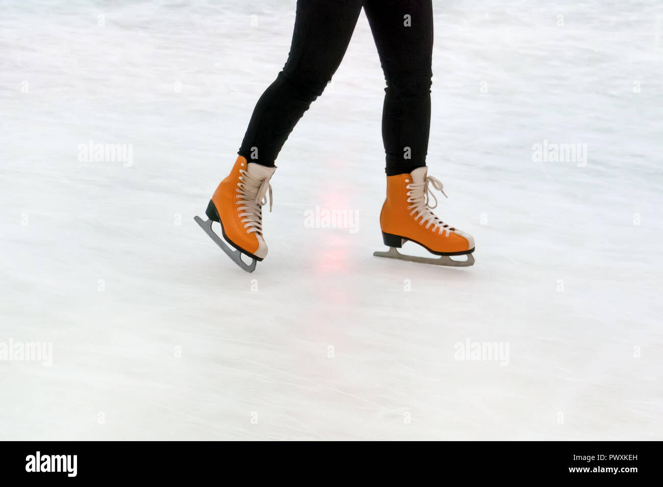 Closeup of legs in skating shoes. Blank copy space. Orange women's skates with reflection on white ice. Stock Photo