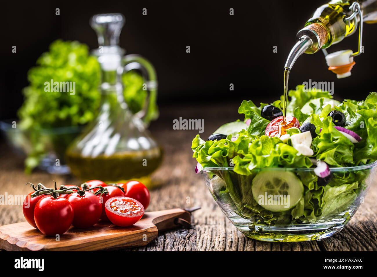 Vegetables lettuce salad with tomatoes onion cheese and olives. Olive oil pouring into bowl of salad. Stock Photo