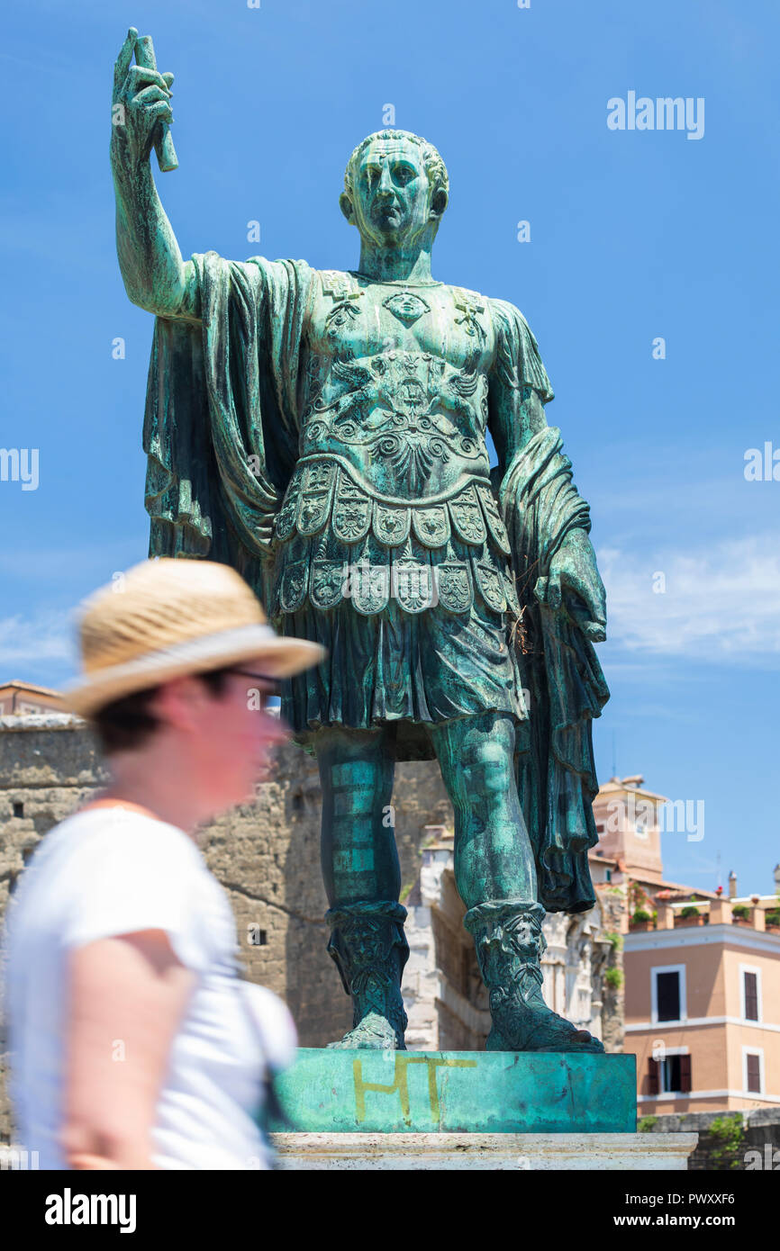 A tourist walks past a bronze statue of Roman Emperor Julius Caesar next to the Forum of August in Rome, Lazio, Italy Stock Photo