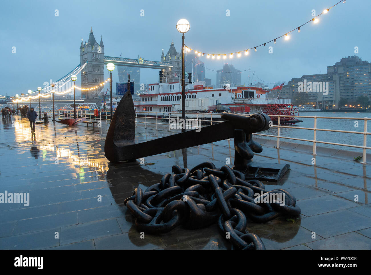 A Wet Early Evening on Butlers Wharf with the Dixie Queen Paddle Steamer, Large Chain and Anchor, Tower Bridge on South Bank River Thames London UK Stock Photo