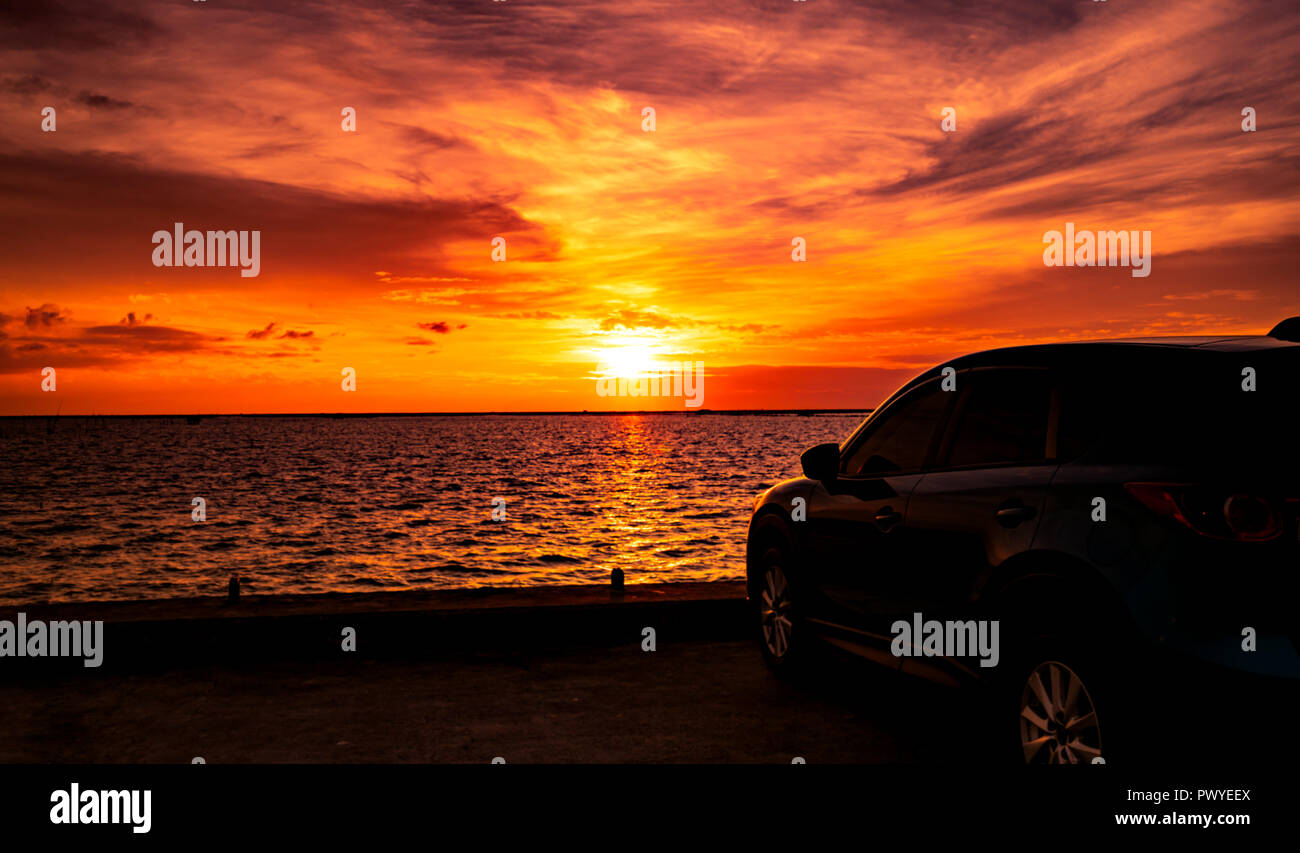 Blue compact SUV car with sport and luxury design parked on concrete road by the sea at sunset. Electric car technology and business. Hybrid auto and  Stock Photo