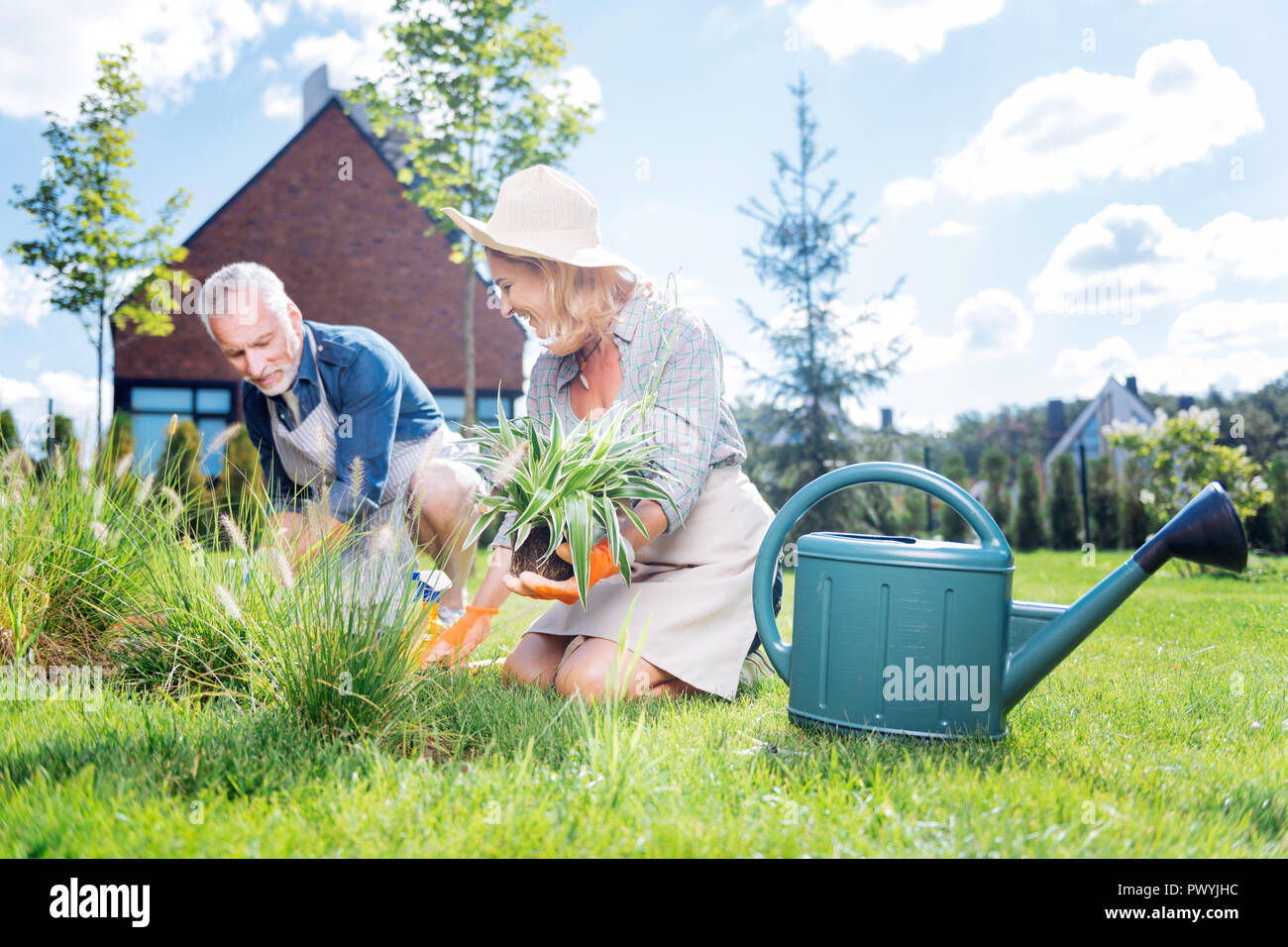 Happy beaming couple sitting hear garden sprinkler while planting flowers Stock Photo