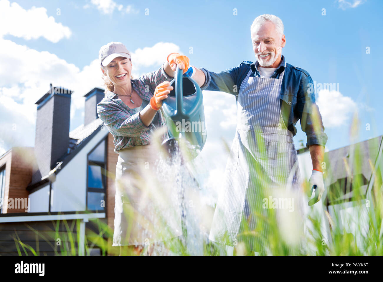 Beaming loving couple holding big garden sprinkler while watering plants Stock Photo