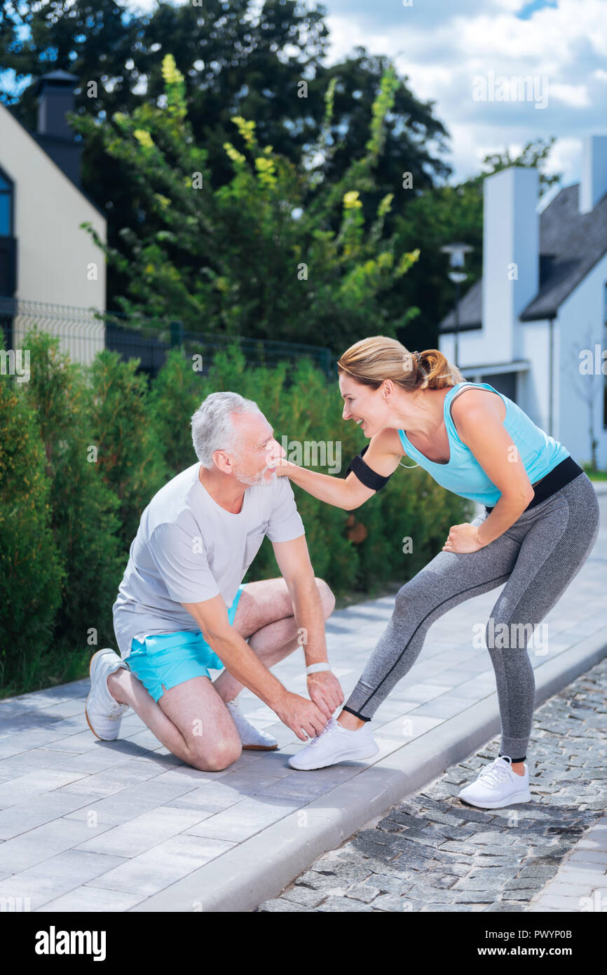 Bearded mans sitting on his knees while lacing sneakers of his slim ...