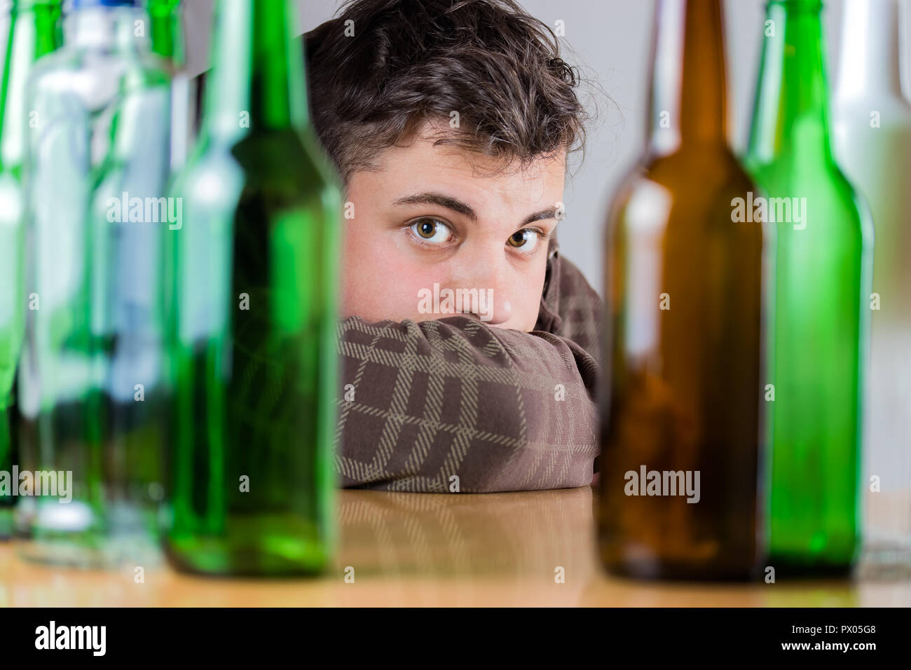 Sad young man behind green and brown glass bottles. Fighting alcohol ...