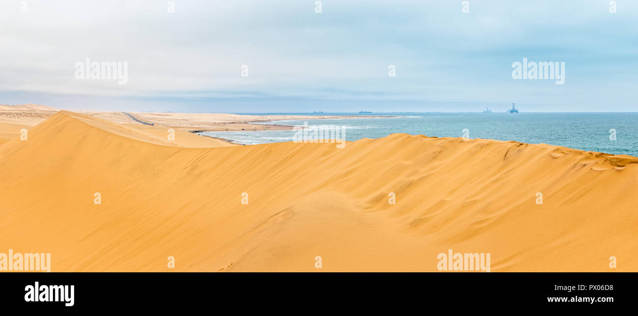 Long yellow sand dune of Kalahari desert and Atlantic ocean shore, with oil rigs and ships on the horizon,close to Swakopmund town, Namibia Stock Photo