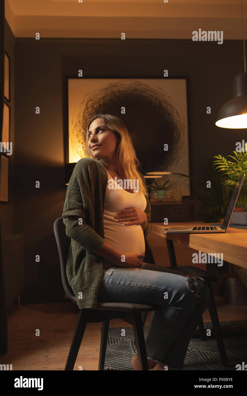 Pregnant woman looking behind while using laptop Stock Photo