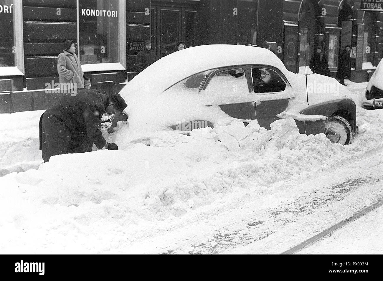 Winter driving in the 1950s. A car owner is trying to clear the car of