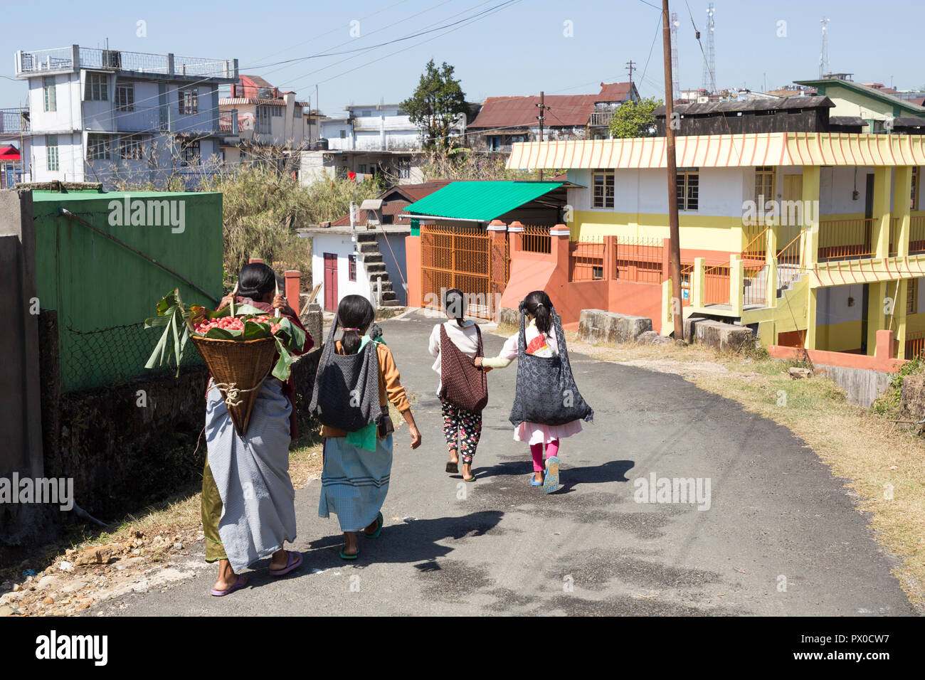 Woman carrying basket of fruit with children walking to market, Mawsynram, Meghalaya, India Stock Photo