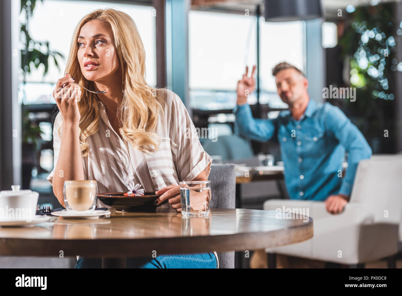 attractive woman eating dessert with flower in cafe, man gesturing to waiter on background Stock Photo