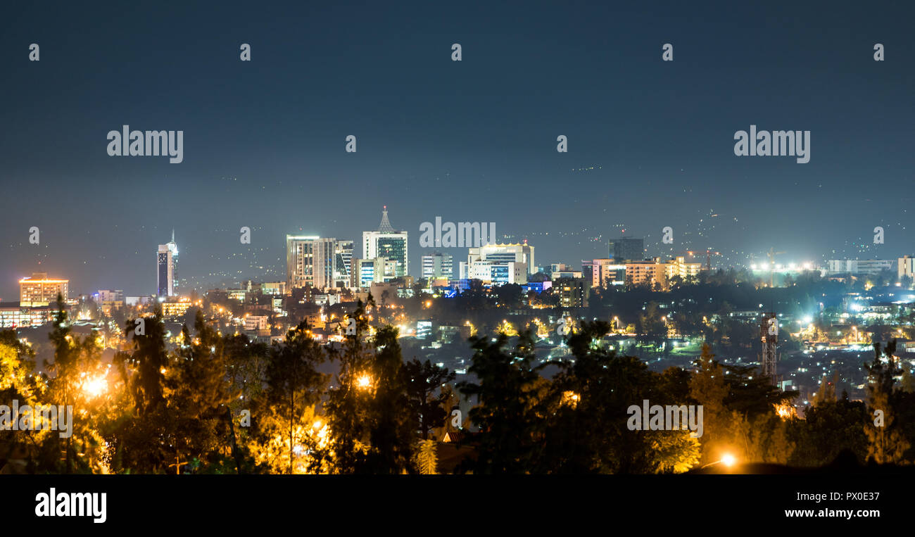 A panoramic view of Kigali city skyline lit up at night, under a deep blue evening sky with the glow of streetlights Stock Photo
