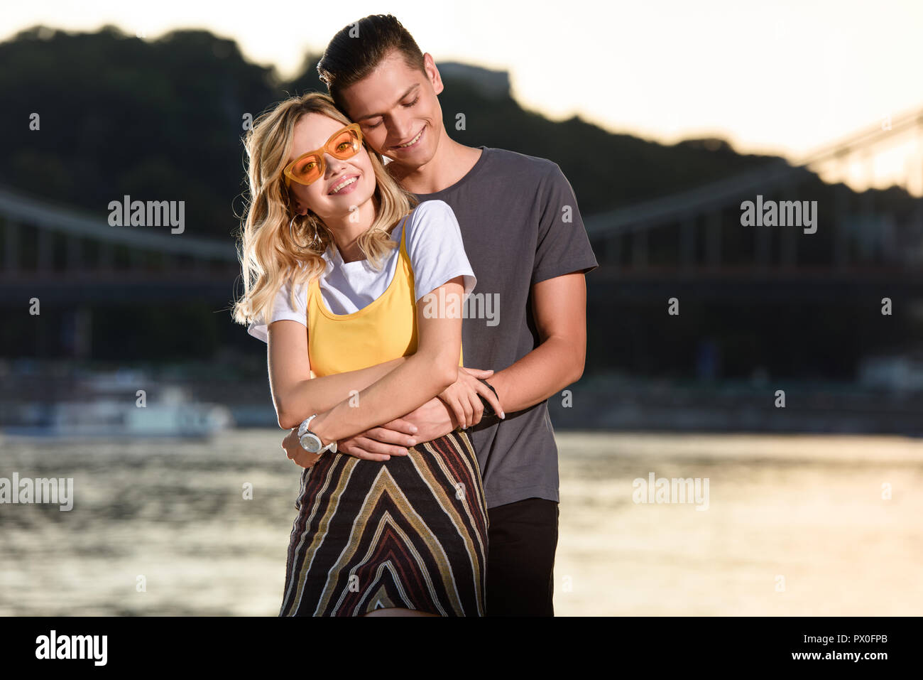 happy boyfriend hugging girlfriend on river beach in evening Stock Photo