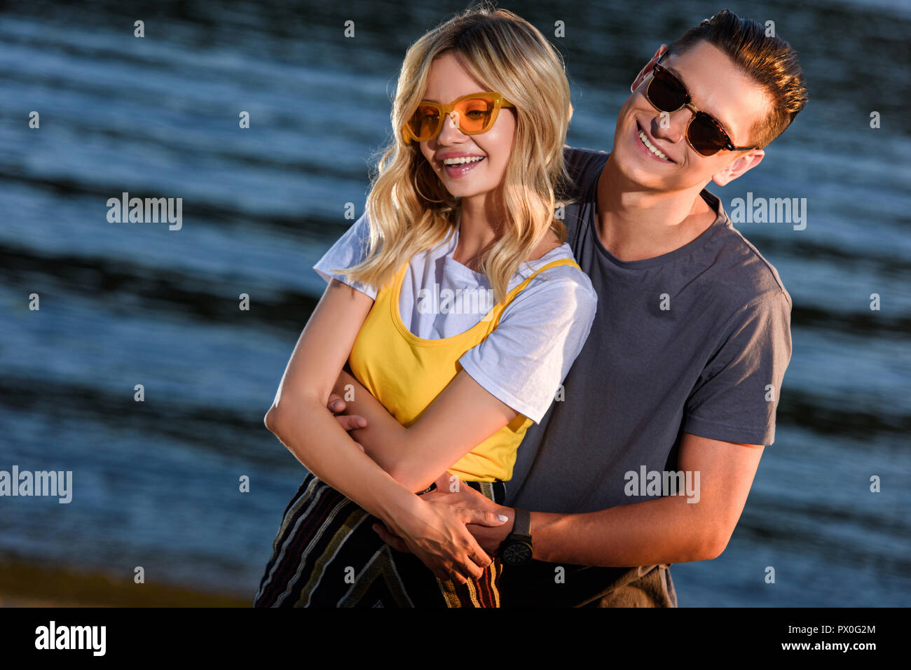 cheerful boyfriend cuddling girlfriend on river beach in evening Stock Photo