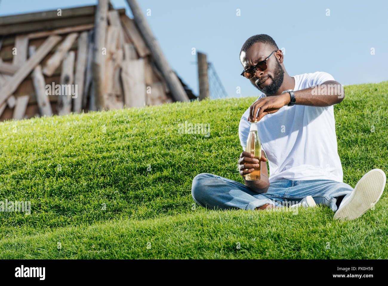 handsome african american man opening soda bottle on green hill Stock Photo