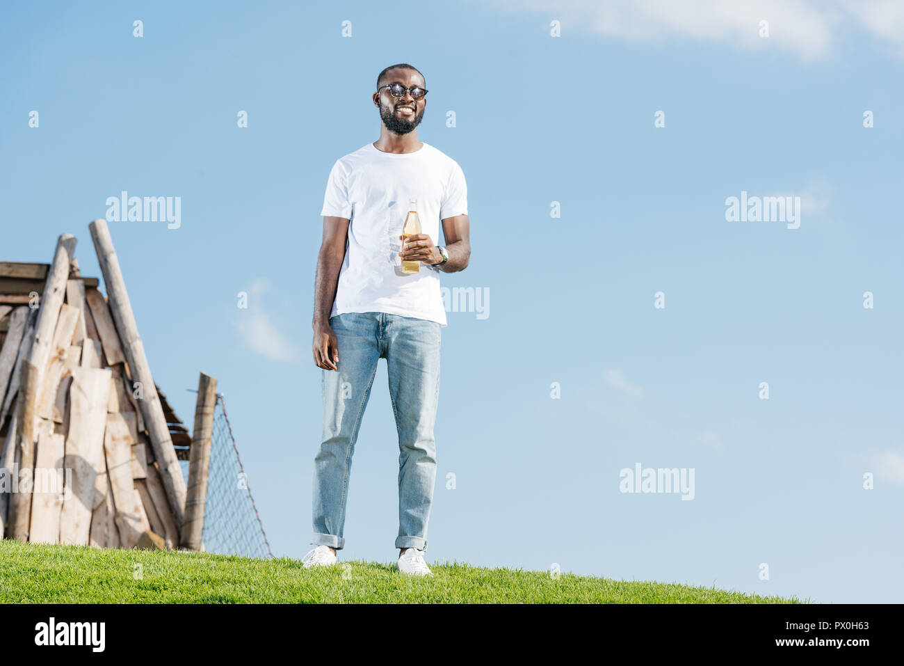 handsome african american man standing with soda in glass bottle on green hill Stock Photo