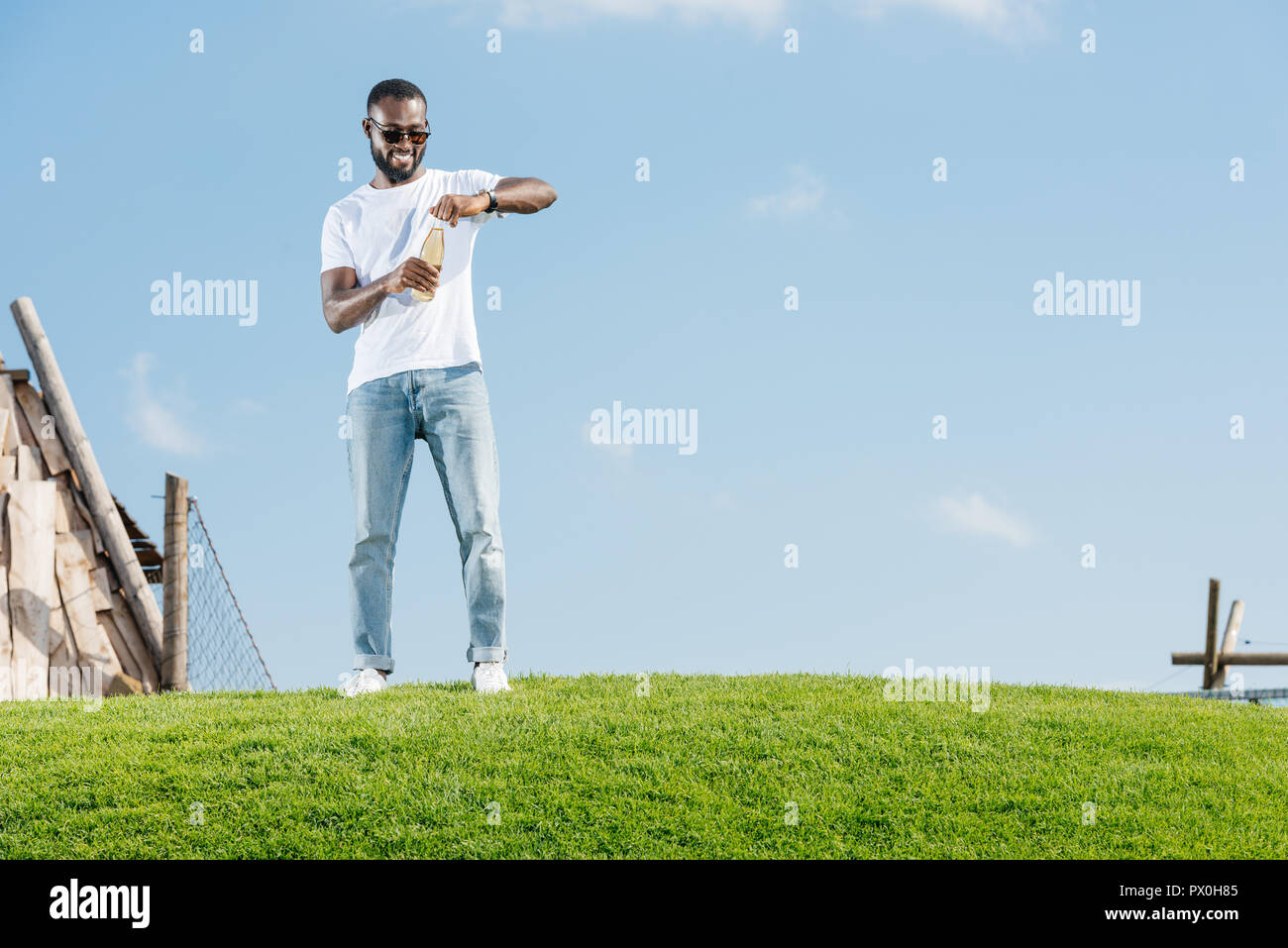 happy handsome african american man opening soda bottle on green hill Stock Photo