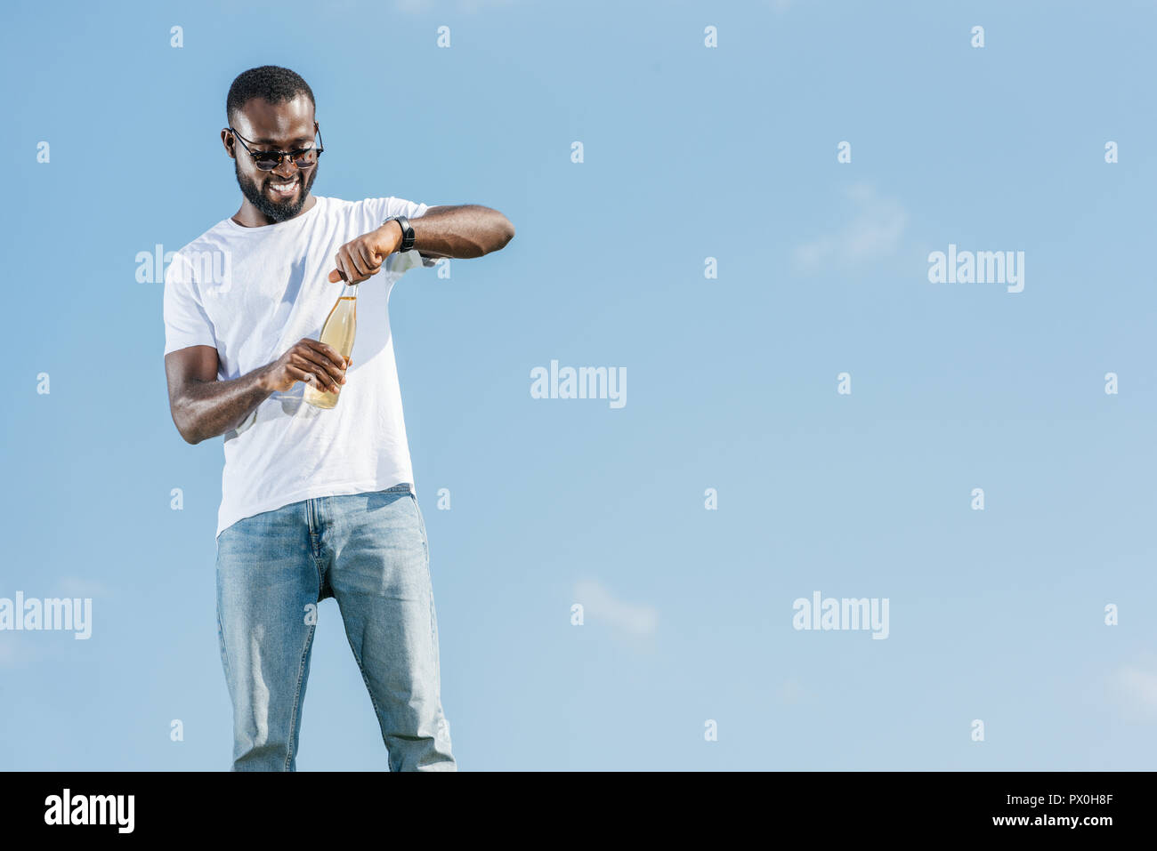 happy handsome african american man opening soda bottle against blue sky Stock Photo