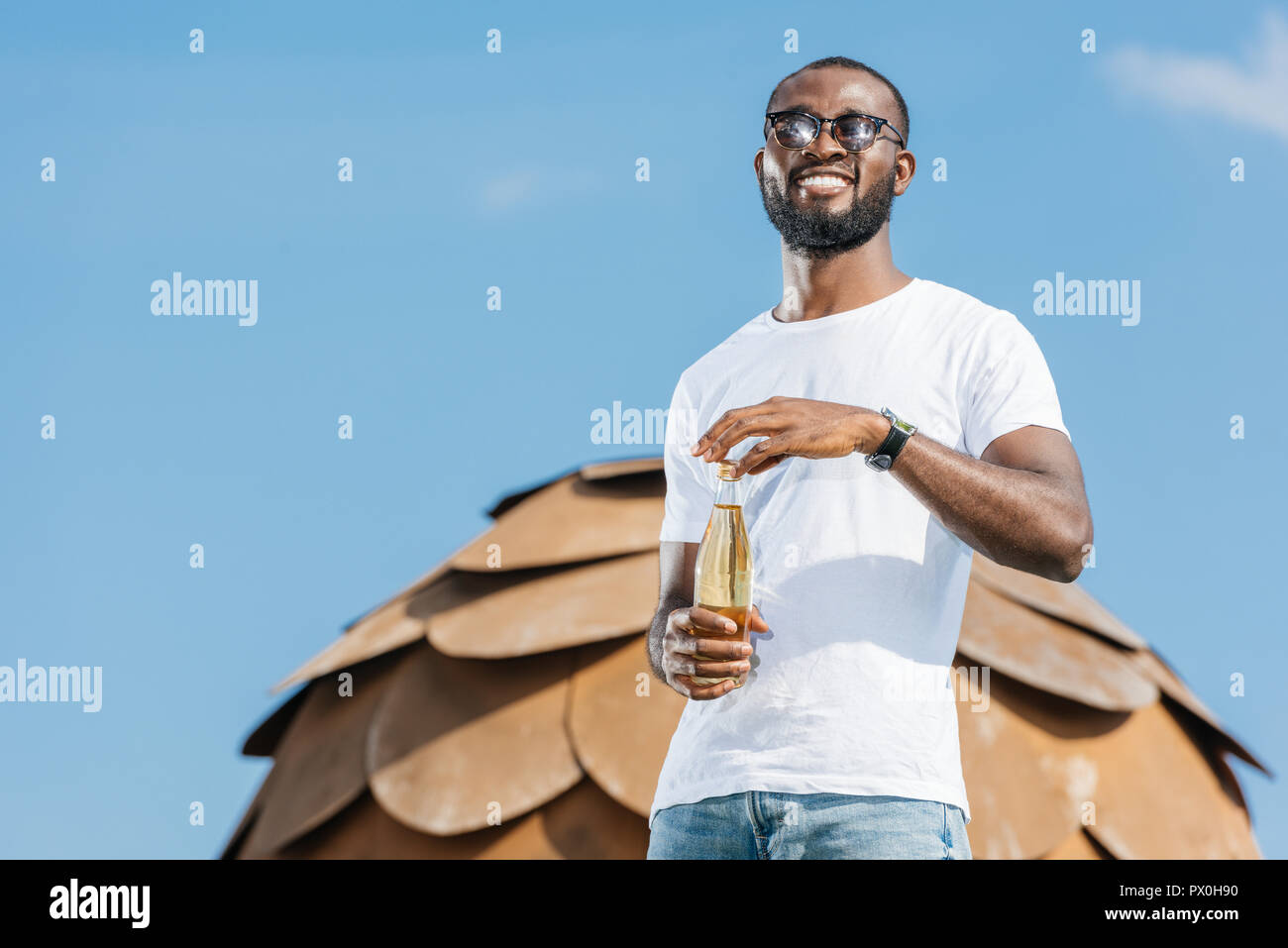 smiling handsome african american man opening soda bottle against blue sky Stock Photo
