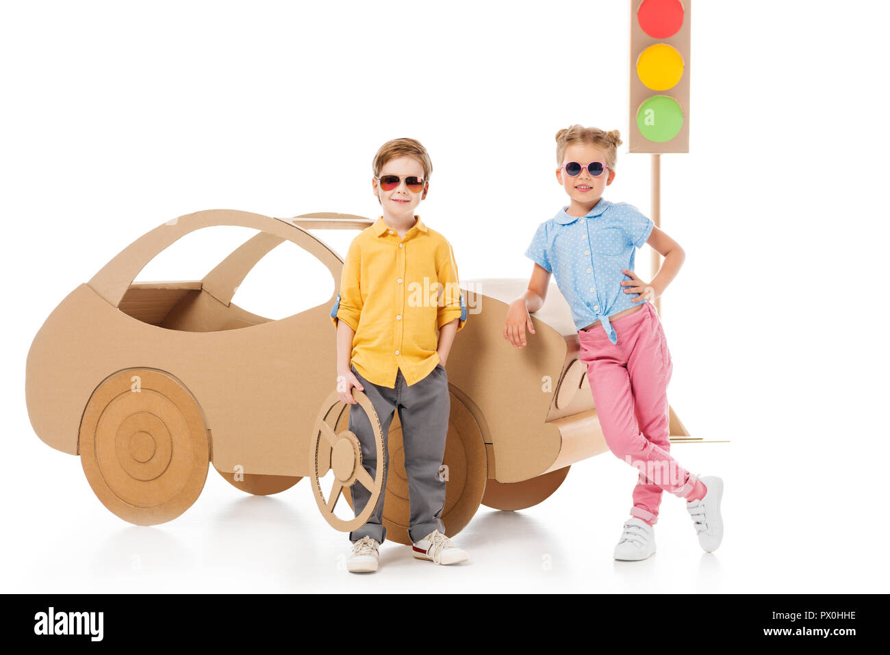 stylish children in sunglasses posing near cardboard car and traffic lights, on white Stock Photo