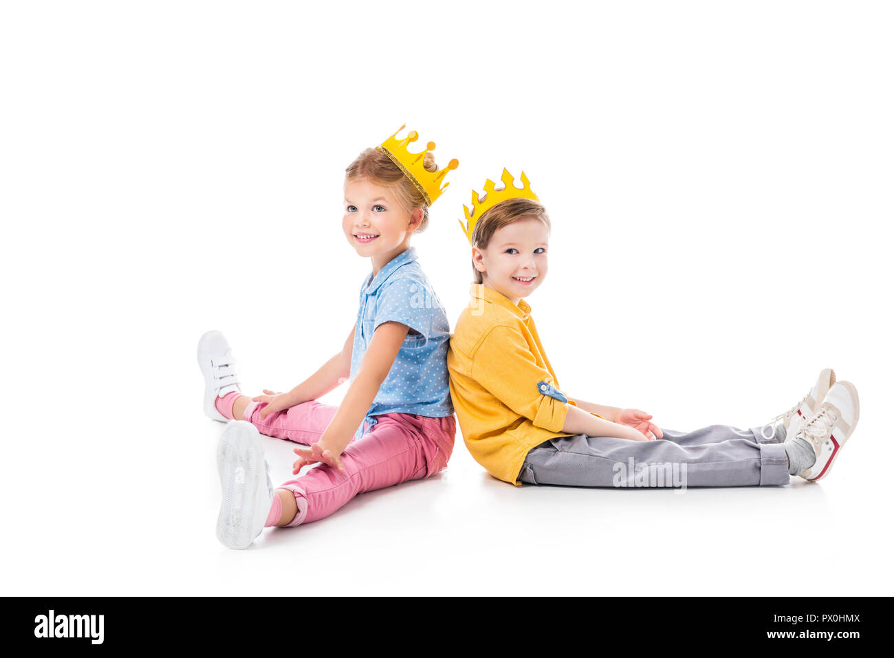 smiling friends in yellow paper crowns sitting back to back, isolated on white Stock Photo